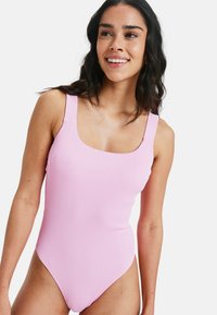 Vaaleanpunainen ribbikuvioinen uimapuku, jossa on leveät hihnat, neliönmuotoinen pääntie ja korkealle leikatut lahkeet, esittelee tekstuuripintaista kangasta.