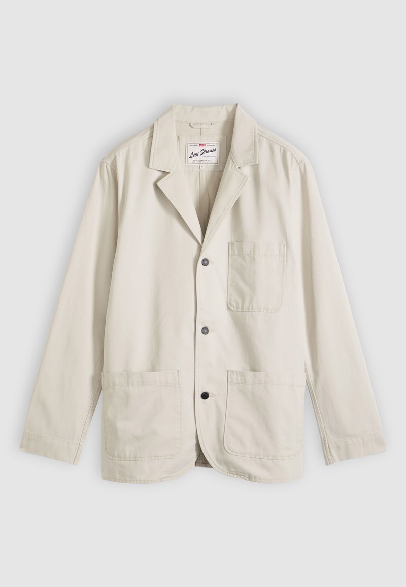 Blazer décontracté beige avec trois boutons sur le devant, une poche poitrine, deux poches plaquées inférieures et un col cranté, posé à plat sur un fond gris.