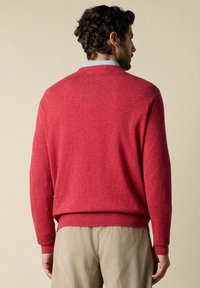 Roter Strickpullover mit weicher Textur, Rundhalsausschnitt und gerippten Bündchen, kombiniert mit hellen Cordhosen.