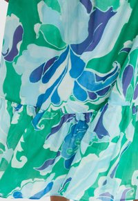 Il vestito floreale presenta un tessuto leggero e fluido in tonalità di verde e blu, con un orlo a volant a strati e grandi motivi floreali morbidi.