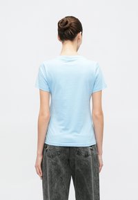 Ανοιχτό μπλε κοντομάνικο μπλουζάκι από μαλακό βαμβακερό ύφασμα. Διαθέτει στρογγυλή λαιμόκοψη και λεία υφή. Φορεμένο με σκουρα, ξεθωρι�ασμένα τζιν.