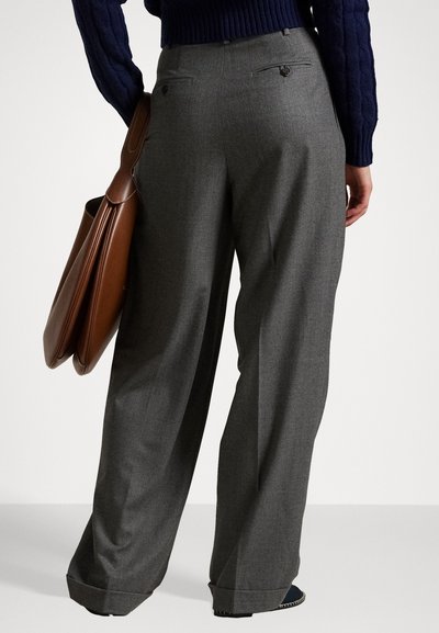 Graue, maßgeschneiderte Hosen mit hoher Taille, weitem Bein und zwei Gesäßtaschen mit Knopfverschlüssen. Begleitet von einer braunen Ledertasche.