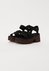 Zwarte platform sandalen met dikke bruine zolen, voorzien van twee brede banden en enkelbanden met klittenbandsluitingen.