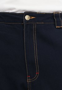 Navy blue fabric pants featuring gold stitching, a gold button closure, and red accent stitching along the seams. Classic design with pockets.