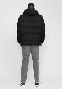 Svart puffjacka med hög krage och horisontellt quiltat mönster, i kombination med grå jeans och svart-vita sneakers.