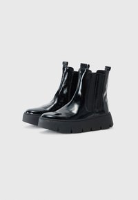 Bottines en cuir verni noir avec des panneaux latéraux élastiques, des pointes arrondies et une semelle en caoutchouc noir épaisse et texturée. Design moderne et épuré.
