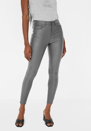 Woman wearing grey high-waist faux leather skinny pants, grey sleeveless top with "DO MORE" text, and black heeled sandals.
