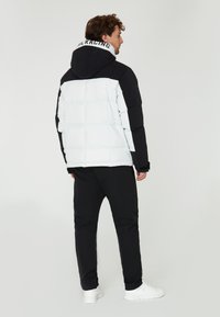 Vit och svart vadderad jacka med huva, med en logotyp på kragen. Kombinerad med svarta byxor och vita sneakers.