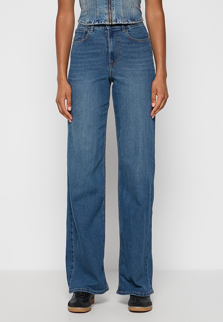 Breda ben blå denimjeans med hög midja, fem fickor och sömnadsdetaljer. Texturerad tyg med en klassisk finish.