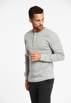 Graues Langarm-Henley-Shirt mit rundem Ausschnitt, fünf vorderen Knöpfen und gerippten Bündchen, kombiniert mit dunklen Hosen.