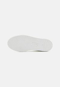 Semelle de chaussure blanche en caoutchouc avec des rainures texturées, arborant un logo circulaire et des inscriptions pour la taille et l'origine. Design lisse et minimaliste.