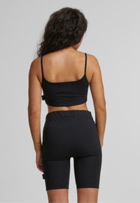 Svart, tettsittende crop top med spaghetti-stropper og matchende høy midje biker-shorts. Begge plaggene har et glatt, elastisk stoff.