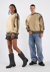 Beige, oversized, gespoten sweatshirts van katoen, gecombineerd met een zwarte denim minirok en zwart laarzen tot de knie met metalen accenten.
