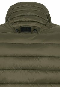 Padded Jacke in Olivgrün mit hohem Kragen, subtilem Steppmuster und einem Etikett auf der Rückseite mit Druckknopfverschluss.