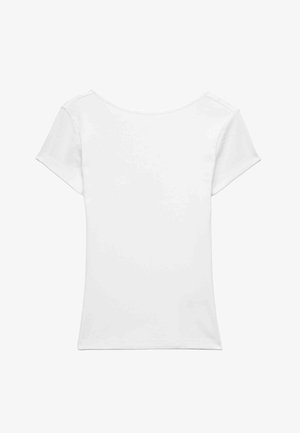 Kobieta w prostym, białym, dopasowanym T-shircie z krótkim rękawem i jasnoniebieskich dżinsach, ze złotymi kolczykami kołami i rozpuszczonym brązowym włosami.