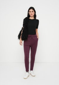 Top nero a maniche corte, pantaloni della tuta color bordeaux a gamba stretta con coulisse e sneakers bianche. La modella porta anche una borsa nera testurizzata.