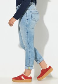 Jeans in denim azzurro chiaro con taglio dritto e orli risvoltati, abbinati a sneakers rosse con dettagli bianchi e suola spessa in gomma color caffè.