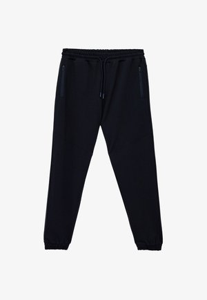 Sorte joggingbukser med elastik i taljen og snøre. Har sidelommer med lynlås og indsnit ved anklerne. Lavet af blødt, strækbart materiale.