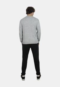 Maglione grigio a maglia con collo rotondo e orlo a coste, abbinato a pantaloni neri a gamba affusolata e sneakers. Visto da dietro.