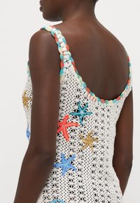 Top corto de crochet blanco con bordados de estrellas de mar coloridos en rojo, azul y dorado, con tirantes de ondas texturizados y multicolores.