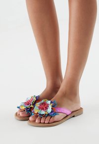 Sandalias florales coloridas con una correa rosa, adornos florales en azul, amarillo y rojo, con una suela de madera plana.