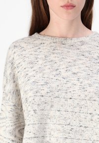 Sweter z jasnej, nakrapianej dzianiny z okrągłym dekoltem i luźnym krojem. Miękka faktura z delikatnymi odcieniami.