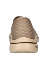 Beige instapschoen met een gestructureerde bovenkant, gevoerde zool en contrasterende donkere accenten langs de zool. Rond gevormd met een lage hak.