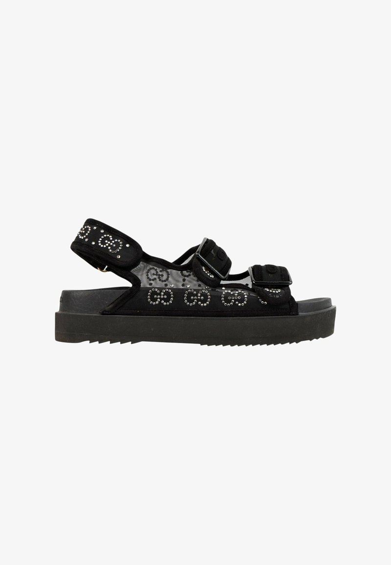 Sandale noire à bout ouvert avec semelle épaisse, doubles brides réglables et motif de logo clouté sur la tige en tissu.