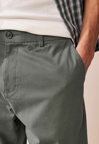 Dunkelgrüne Hose aus glattem Stoff, mit Knopfverschluss, seitlichen Taschen und einem klassischen, tailored Fit.