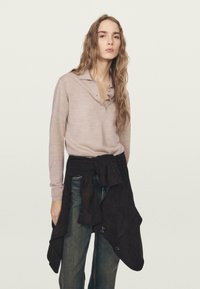 Jasnoróżowa koszulka polo z długim rękawem i kołnierzykiem, zestawiona z ciemnobrązową spódnicą kopertową na niebieskich dżinsach. Gładka tekstura; prosty wzór.