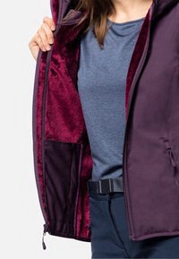 Veste d'extérieur violette avec une doublure en velours bordeaux, équipée d'une poche zippée et d'une chemise bleue en dessous. Texture extérieure lisse.