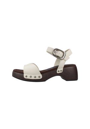 Sandalo in pelle bianca con tacco basso a blocco in legno scuro, cinturino alla caviglia con fibbia argento e dettagli con rivetti metallici sulle cinghie.