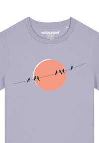 Helles lavendelfarbenes T-Shirt mit einem runden, pfirsichfarbenen Grafik eines Sonnens und fünf schwarzen Vögeln auf einer Schnur, aus weichem Stoff gefertigt.