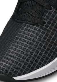 Scarpa sportiva nera con tomaia in rete testurizzata che presenta un motivo esagonale, lacci neri e una suola in gomma bianca come accento.