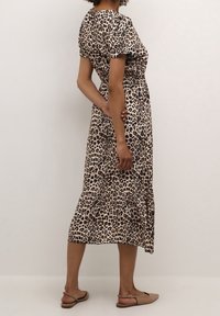 Maxikleid mit Leopardenmuster, kurzen Ärmeln, elastischem Bund und Rüschen-Saum, aus leichtem Stoff; getragen mit beigen flachen Sandalen.