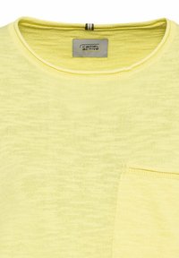 Gelbes T-Shirt mit kurzen Ärmeln, das eine strukturierte Oberfläche, einen runden Halsausschnitt und eine Brusttasche auf der linken Seite aufweist. Markenetikett sichtbar im Inneren.