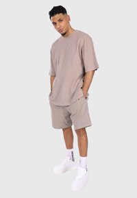 Chemise à manches courtes beige texturée associée à un short assorti. La tenue présente une coupe décontractée et est complétée par des baskets blanches et des chaussettes.