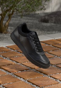 Sorte læder sneakers med en glat overflade, flade snørebånd og en gummisål. Har branding på siden og detaljeret syning.