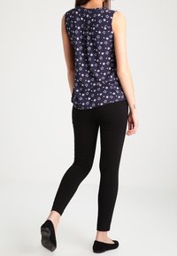 Meriininsininen hihaton toppi, jossa valkoinen tähtikuvio, pleated-taakse yksityiskohta, yhdistetty mustiin kapeisiin housuihin ja mustiin ballerinoihin.