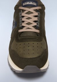 Olive green sneaker featuring a mesh upper, suede accents, perforated toe box, and tan laces. Solid white midsole with textured grey outsole.