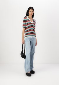 Red, green, and blue striped knit top with a V-neck and short sleeves; paired with light blue straight-leg jeans and chunky black platform shoes.