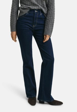 Dunkelblaue ausgestellte Jeans aus Denim mit hoher Taille, sichtbaren Nähten und einem Frontknopfverschluss, kombiniert mit einem grauen Strickpullover.
