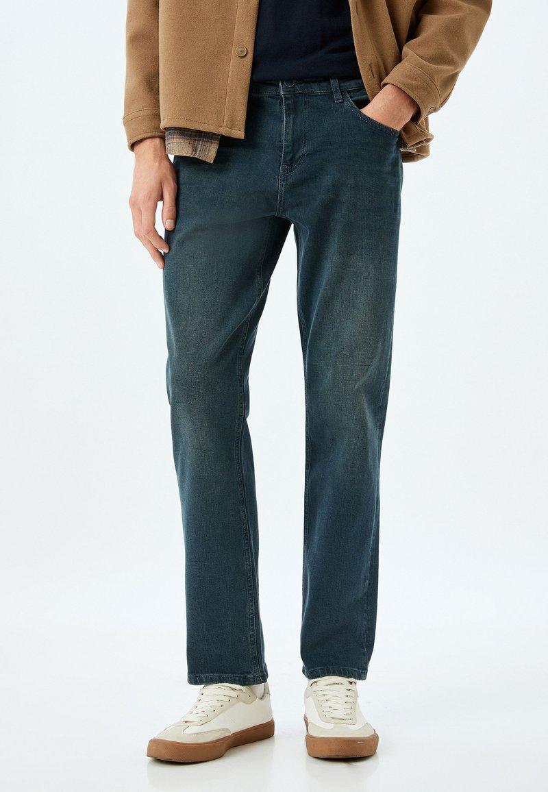 Tummansininen farkkutakki suoranlahkeisella leikkuulla, jossa on klassinen viiden taskun muotoilu ja hienovaraista haalistumista.