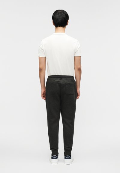 Σκούρα γκρι φόρμες με άνετη εφαρμογή, ελαστική μέση και μανσέτες στα πόδια. Συμπληρώνονται με ένα απλό λευκό t-shirt και λευκά αθλητικά παπούτσια.