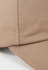 Brown cap featuring a textured fabric with visible stitching and a curved brim, emphasizing the durable material and construction details.