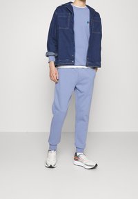 Felpa azzurro chiaro, pantaloni della tuta abbinati e una giacca di jeans blu scuro con quattro tasche. Sneakers bianche con dettagli multicolori.