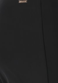 Black dress featuring a smooth, matte texture with a subtle sheen. Gold metallic brand tag located near the neckline.