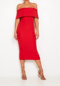 Robe rouge cintrée à épaules dénudées avec une longueur midi. Texture lisse et design structuré. Portée avec des talons nus à lanières.