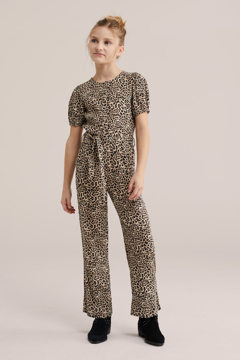 Joven niña de pie vistiendo un mono de estampado de leopardo en color canela y negro con mangas abullonadas y botines negros.