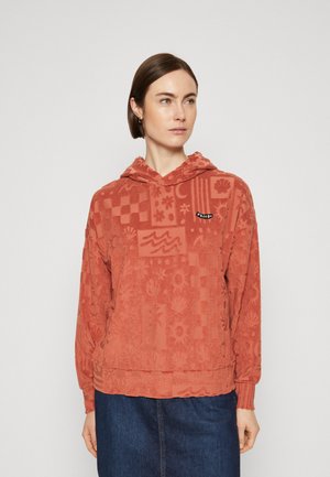 Sudadera de color óxido con un patrón texturizado de flores y formas geométricas. Incluye un bolsillo canguro en la parte frontal y capucha con cordón.